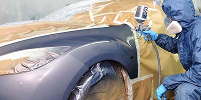 Worker painting car in a paint booth